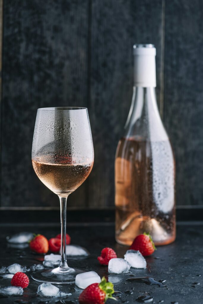 Glass of cooled rose wine, bottle, icecubes and strawberries and raspberries on dark ground